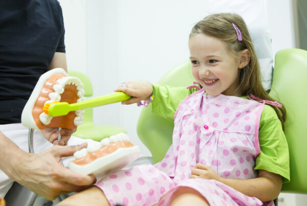 Girl in pediatric dentist's chair toothbrushing a model